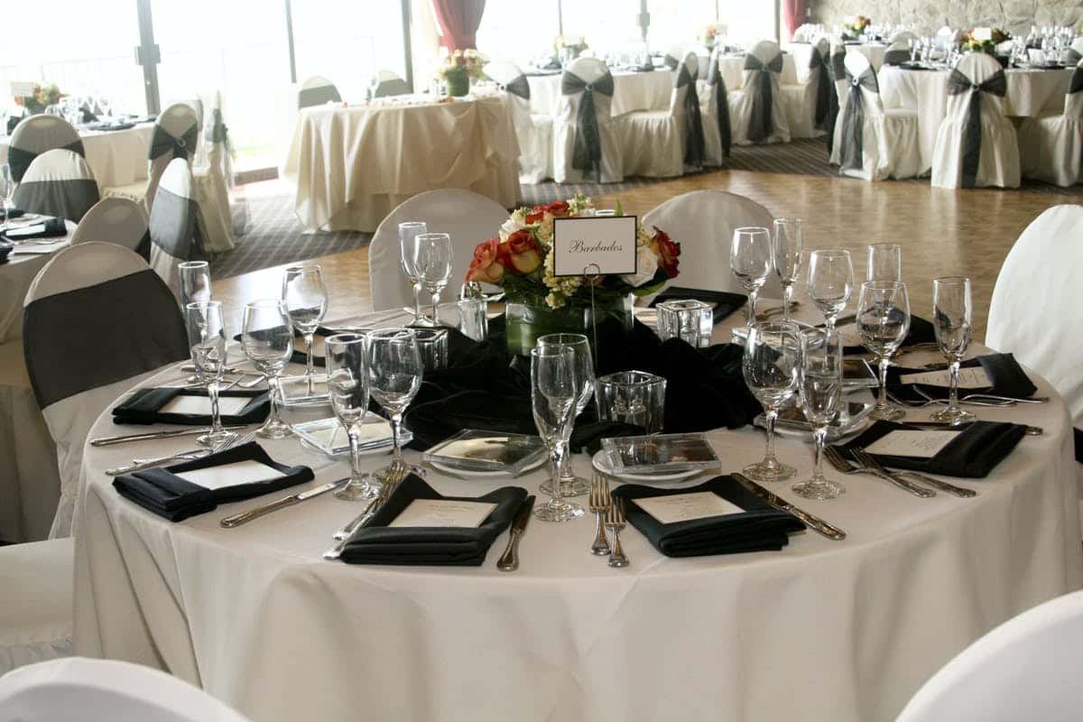 Elegant wedding reception table setting with black chair sashes, formal place settings, and floral centerpiece in a modern ballroom venue