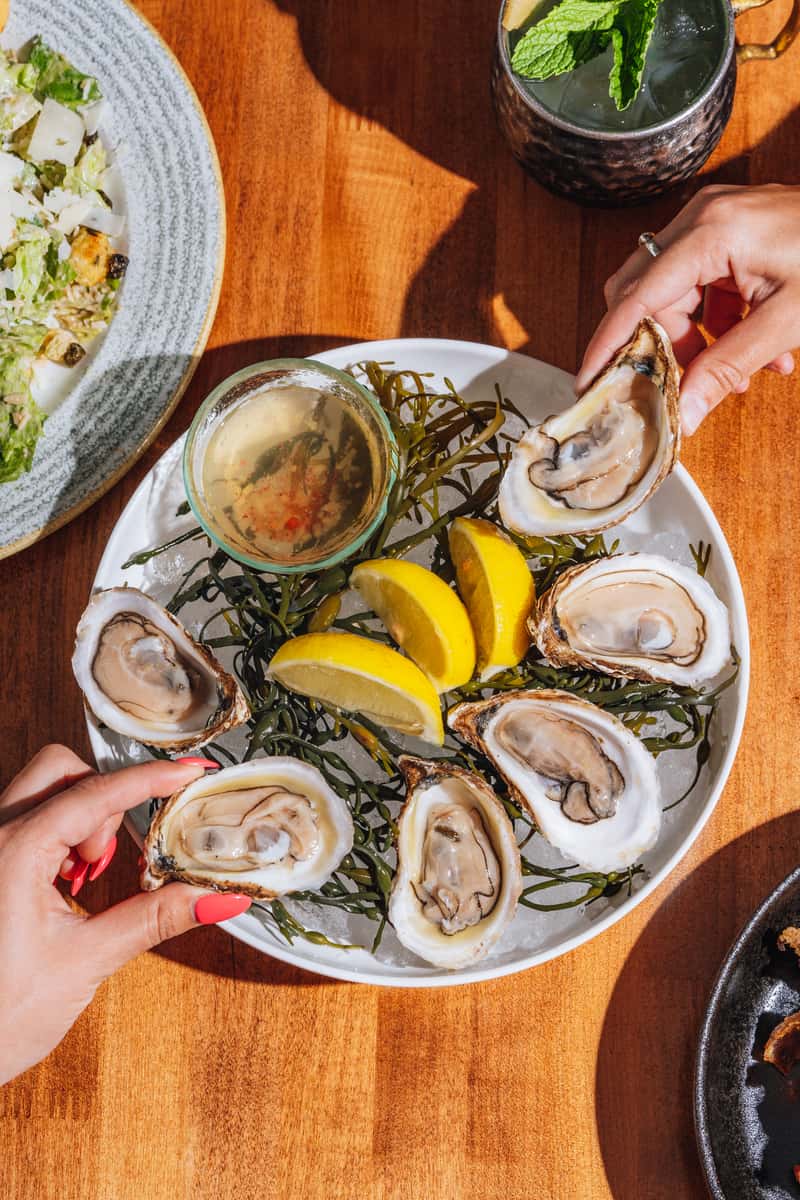 Guests enjoy grabbing these succulent oysters with lemon wedges, presented on a stylish wood table.