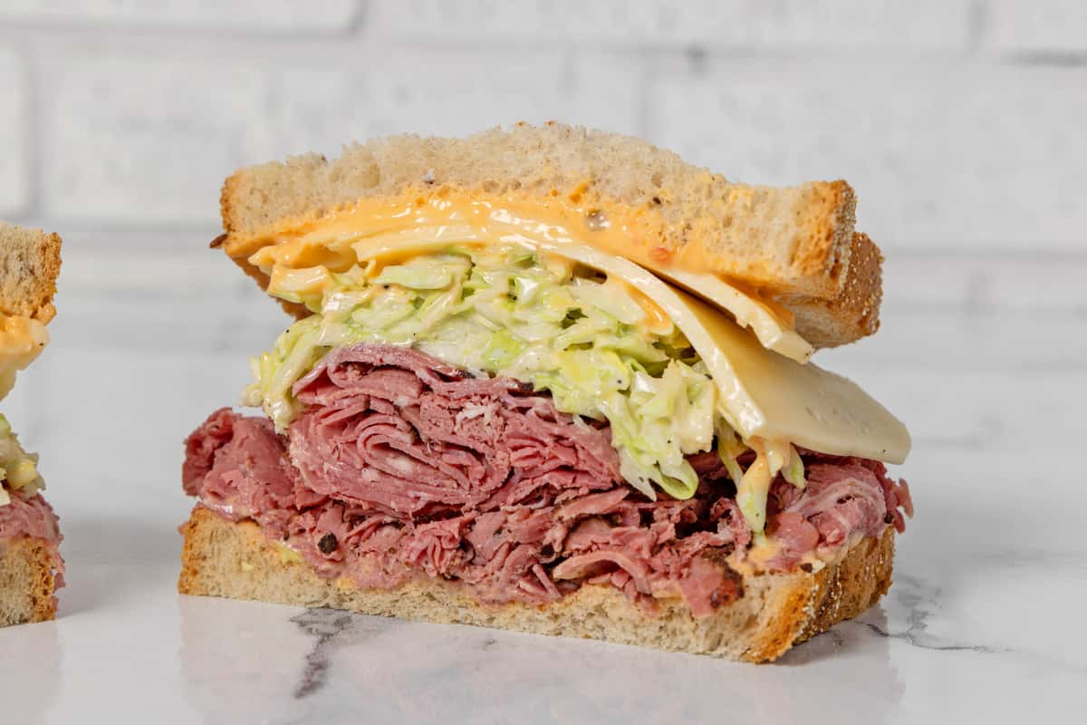 pastrami deli sandwich with melted cheese, coleslaw, and creamy dressing on rye bread
