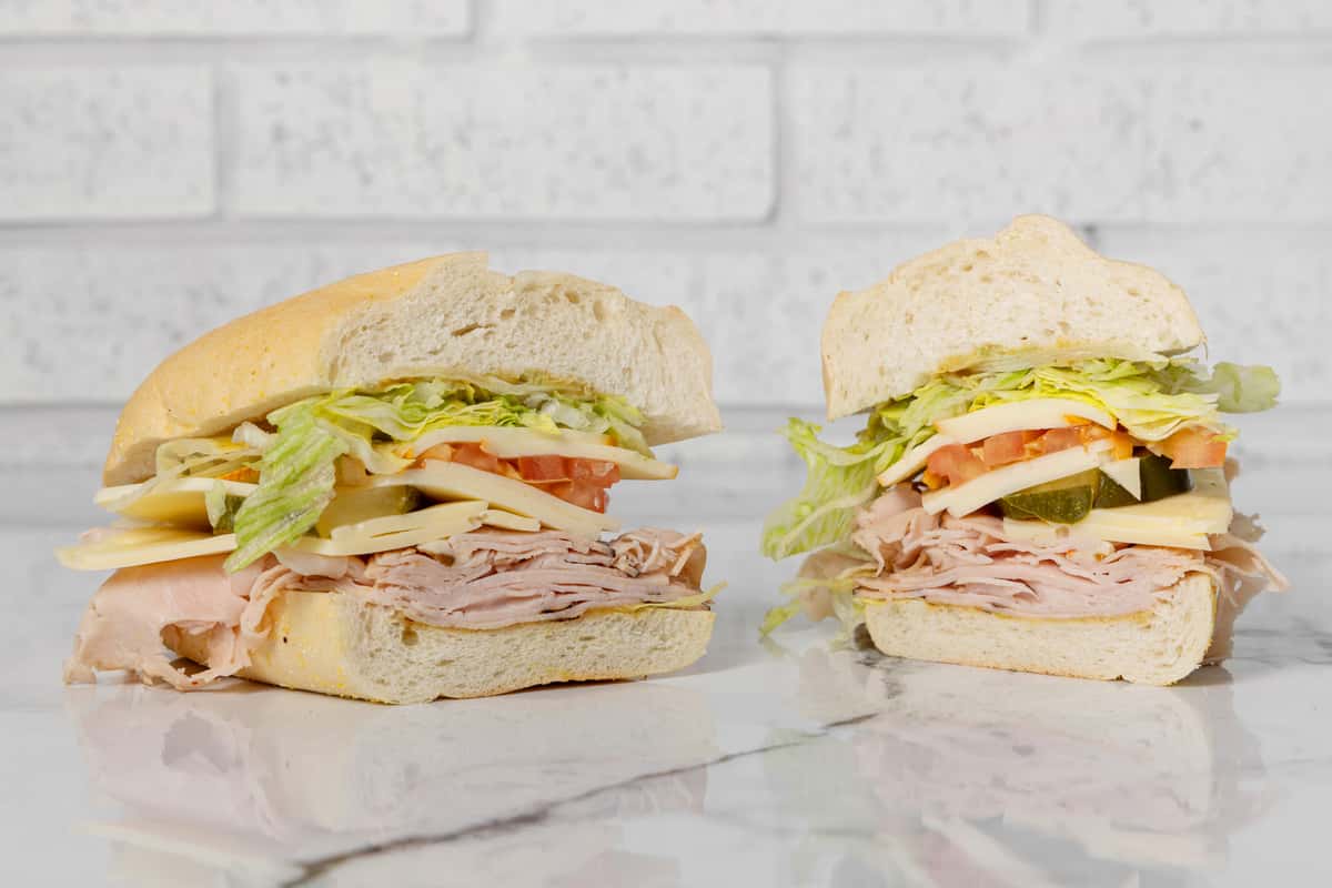 Turkey and cheese deli sandwich halves with lettuce, tomato, pickles, and onions on a soft hoagie roll, served on a marble counter