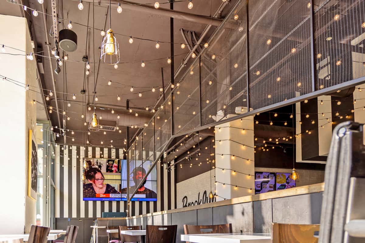 Warm modern restaurant interior with string lights, striped accent wall, and casual dining tables at Brooklyn Square