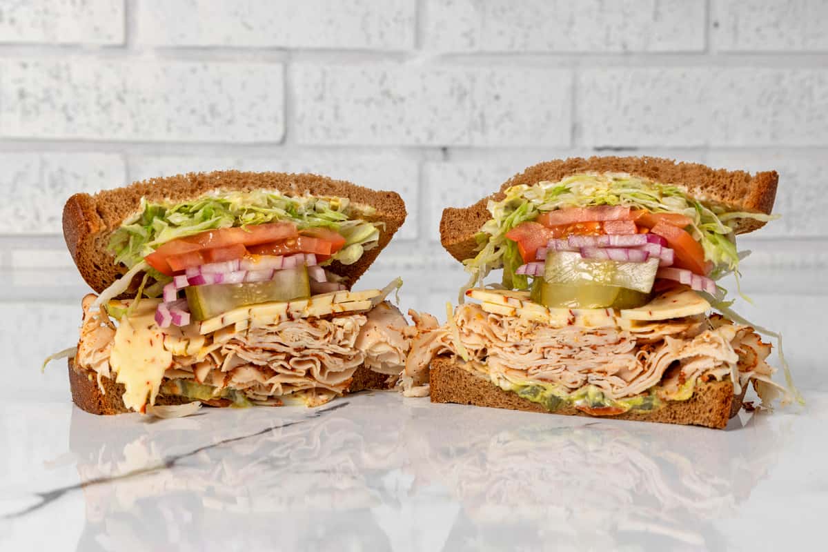 Turkey deli sandwich halves with cheese, lettuce, tomato, pickles, and onions on whole grain bread