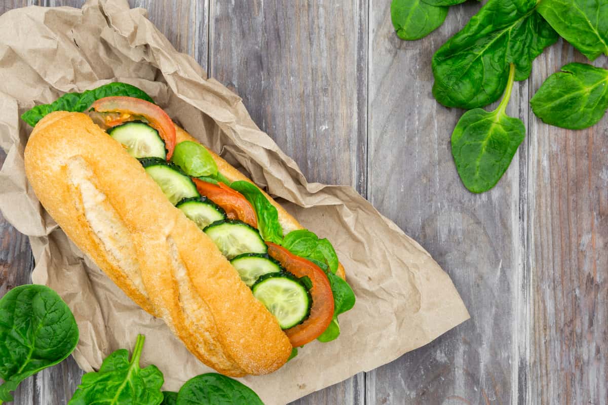 A veggie sandwich featuring fresh sliced cucumbers and tomatoes arranged on a baguette. This fresh image has great appeal as a header logo, as the website page suggests.