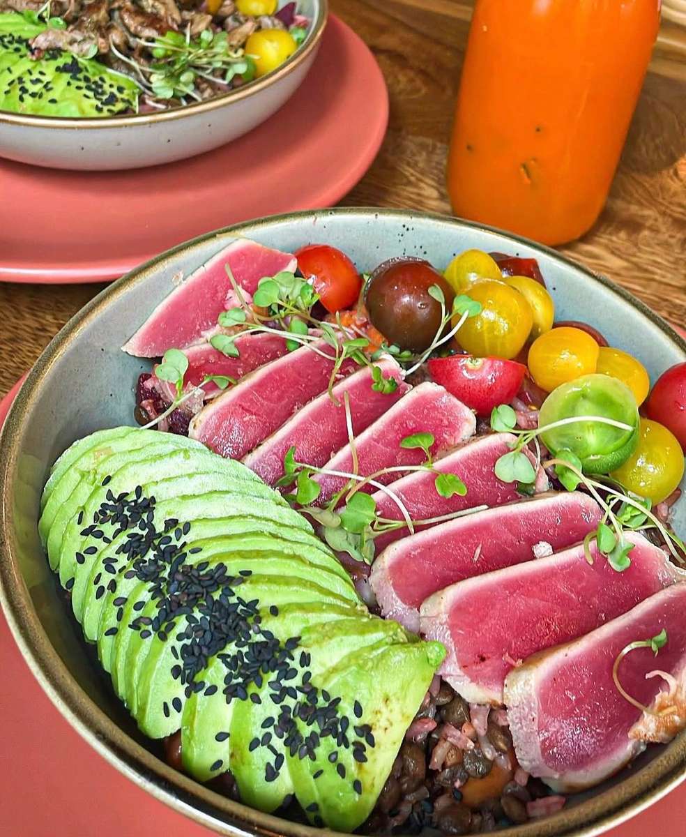 Vibrant ahi tuna poke bowl with seared tuna slices, heirloom cherry tomatoes, microgreens, and sliced avocado topped with black sesame seeds, served over a bed of grains and legumes in a ceramic bowl.