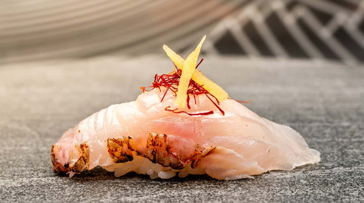 Nigiri sushi with white fish, topped with thin yellow slices and red saffron threads on a grey surface.
