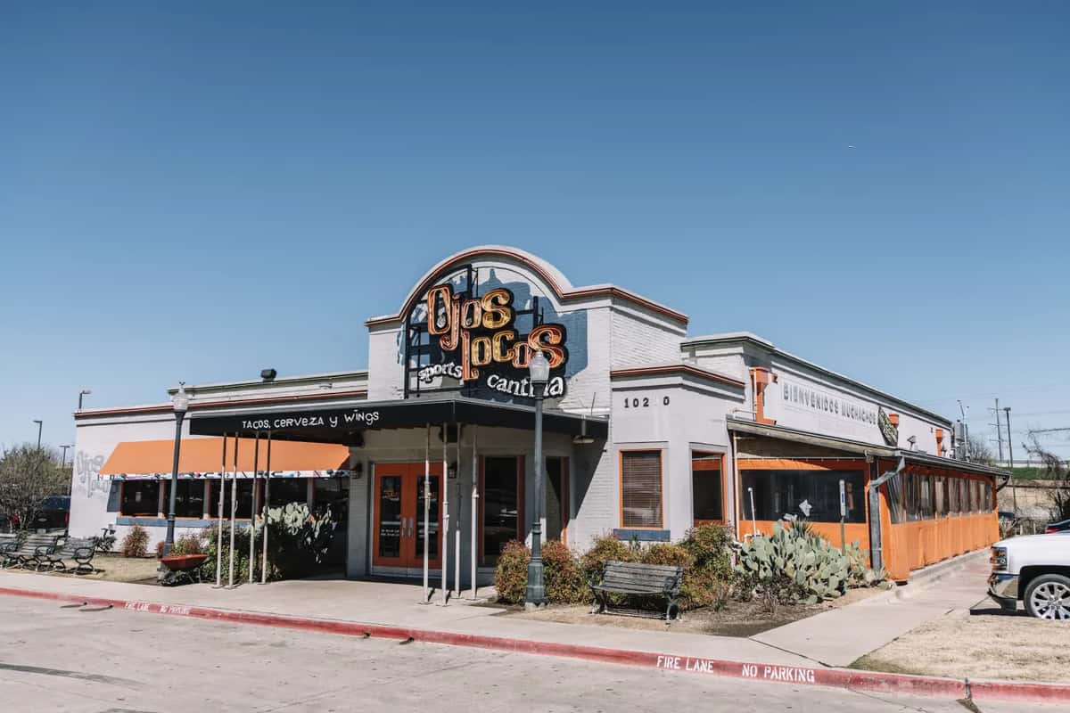 OjOs Locos Sports Cantina exterior with orange awnings and signage reading tacos, cerveza y wings under blue sky
