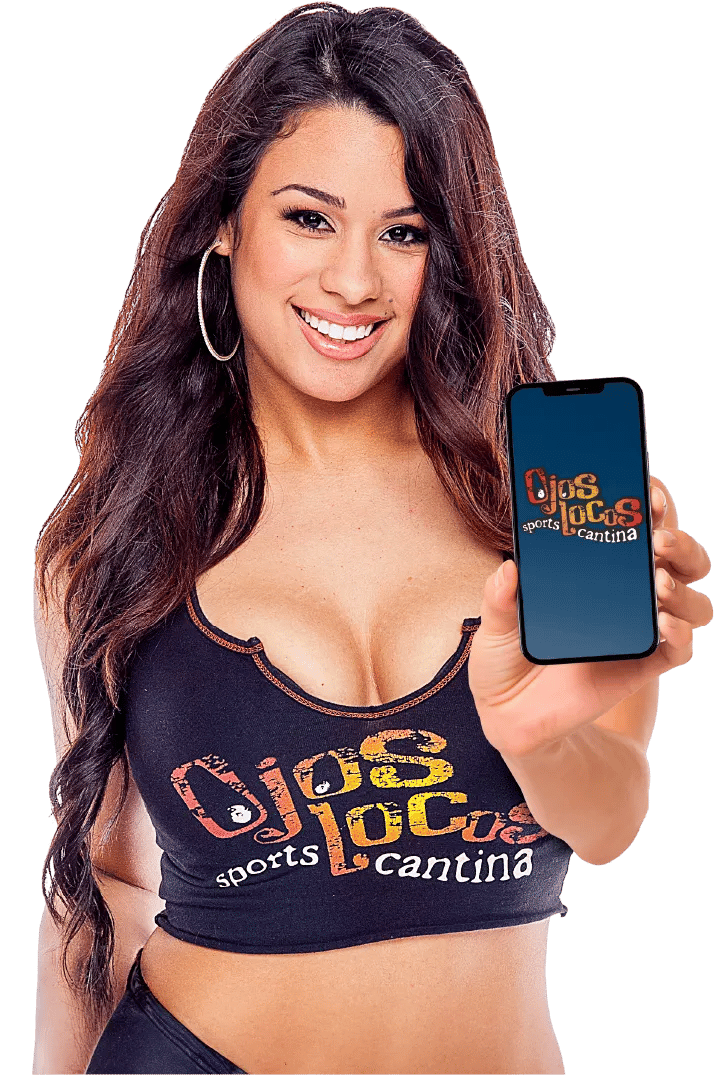 A smiling woman wearing an "Ojos Locos Sports Cantina" crop top is holding up a smartphone displaying the restaurant's logo on the screen. She has long dark hair, hoop earrings, and is posing against a plain white background, presenting the phone toward the viewer.