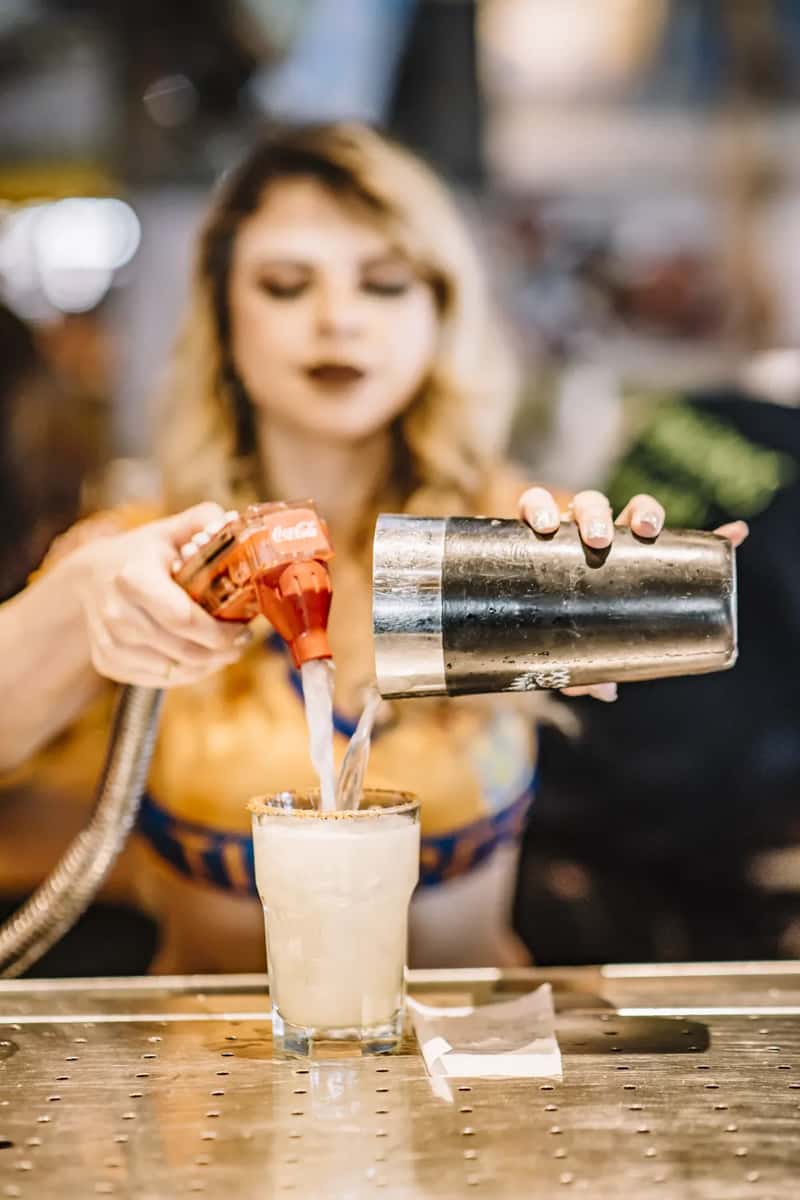 Bartender pouring frozen margarita into a salt-rimmed glass behind the bar counter