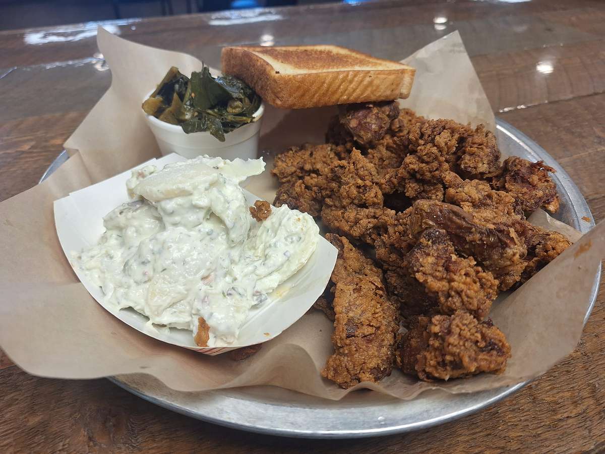 Crispy fried chicken livers served with collard greens, toast, and a side of creamy potato salad on a metal tray