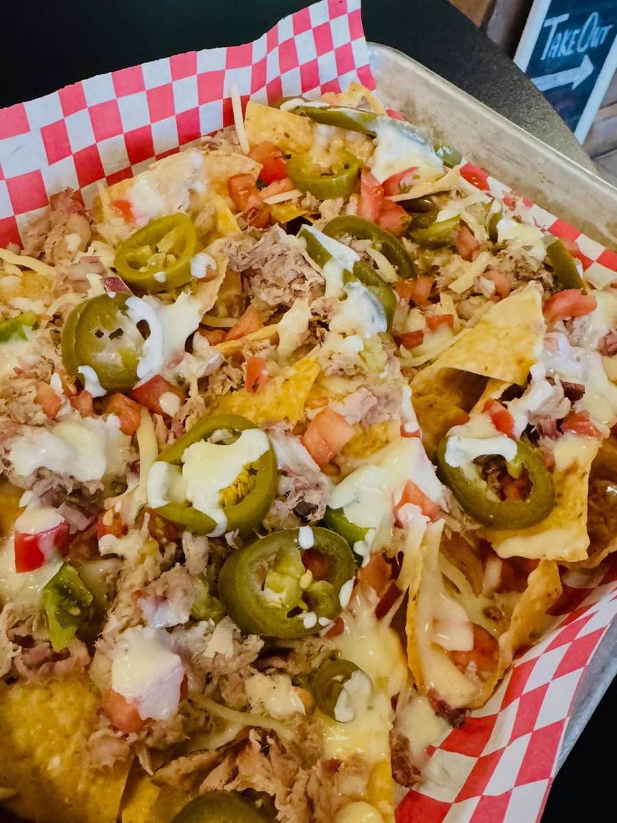 Loaded nachos topped with pulled pork, melted cheese, jalapeños, and fresh pico de gallo in a red checkered basket