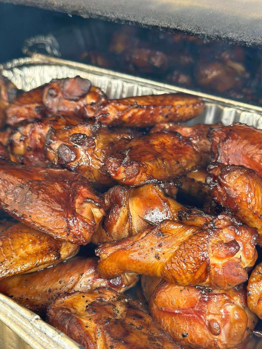 Smoked chicken wings with caramelized barbecue glaze stacked in a tray inside a smoker, showcasing rich color and crispy skin