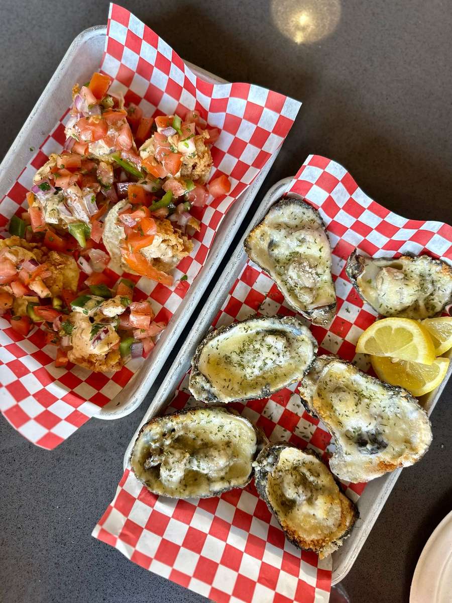 Charbroiled oysters topped with garlic butter and herbs served with lemon wedges on a seafood restaurant tray