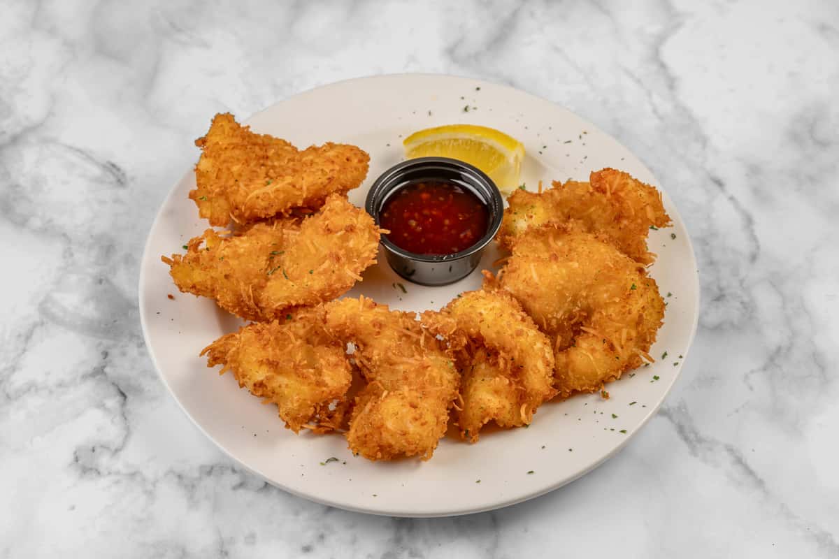 Plate of golden-brown coconut shrimp served with a wedge of lemon and a side of sweet chili dipping sauce — a crispy seafood appetizer perfect for tropical or coastal-inspired dining.