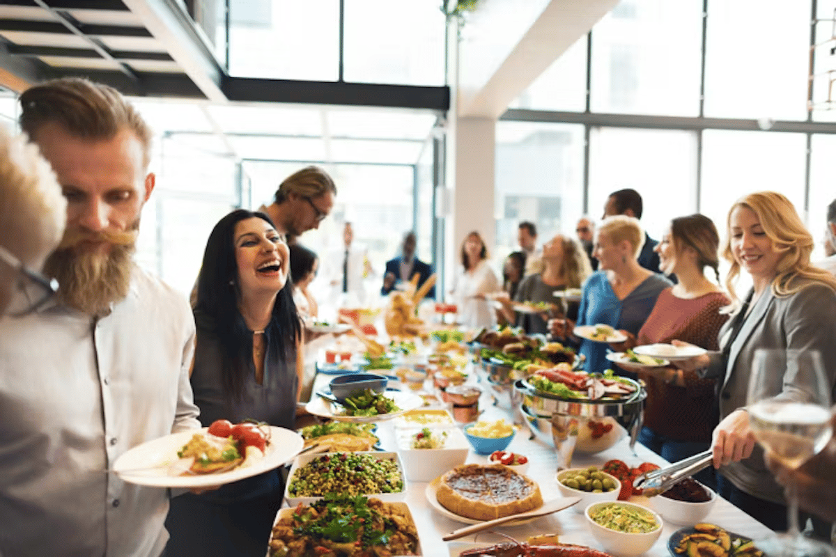 A lively buffet gathering with people smiling, serving themselves a variety of dishes in a bright, modern venue.