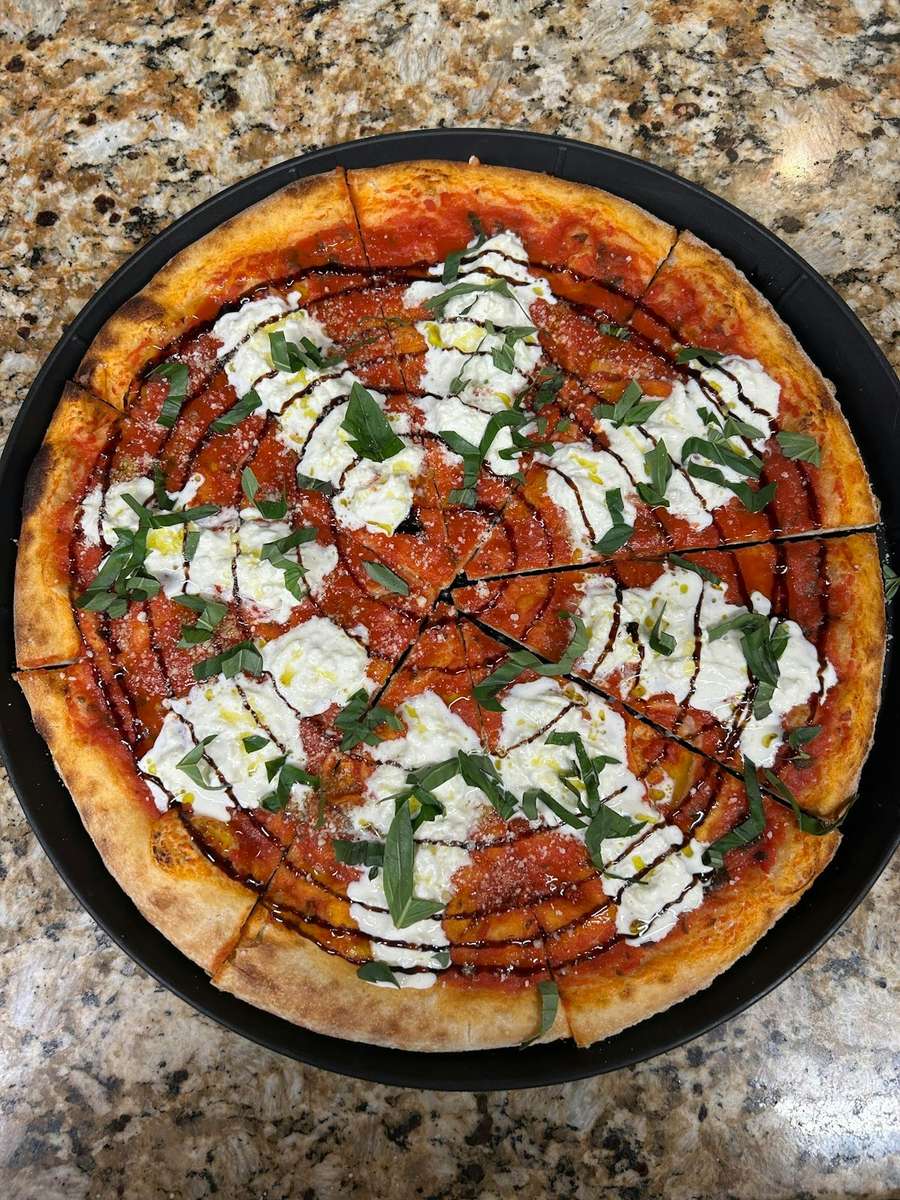 Freshly baked pizza topped with stracciatella, tomato sauce, fresh basil, balsamic glaze, and a drizzle of olive oil