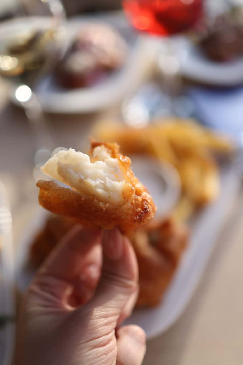 Close-up of flaky white fish inside crisp golden batter, with freshly cooked chips blurred in the background.