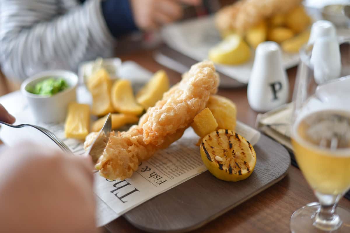 Freshly battered fish and golden chips served at the table with sauces and a grilled lemon.