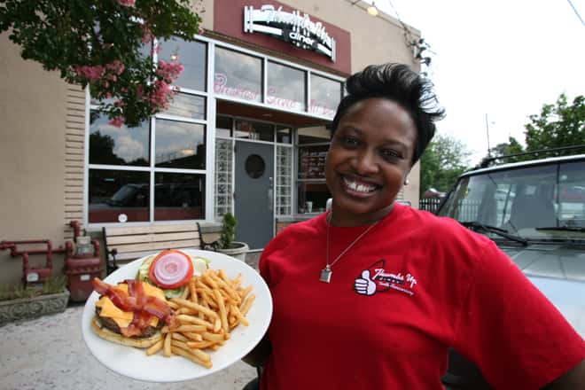 woman smiling holding a bacon cheeseburger with french fries outside the business 