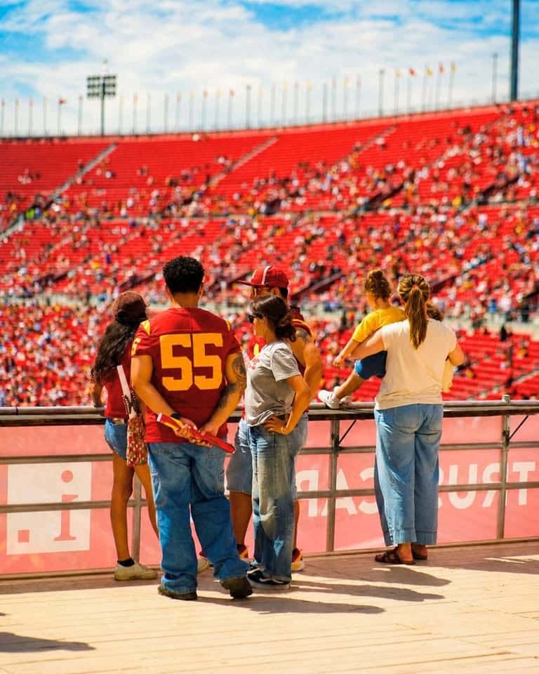 A few people in red sports jerseys standing at a railing in front of rows of red stadium seats
