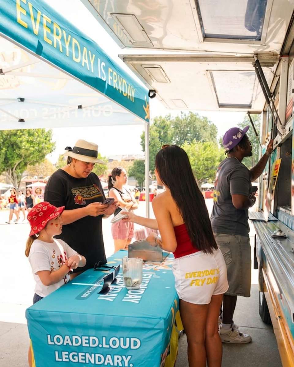 Guests chatting and lining up at an outdoor food truck service window on a sunny day
