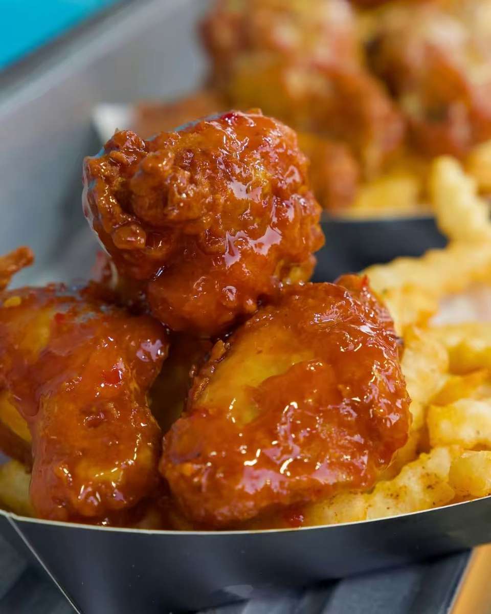 Close-up of glazed, sauced fried chicken pieces resting on a bed of golden fries