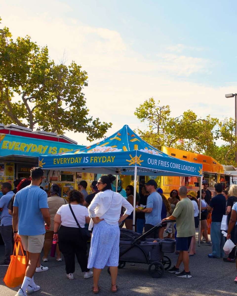 Crowd of people gathered outdoors beneath colorful event tents on a sunny day