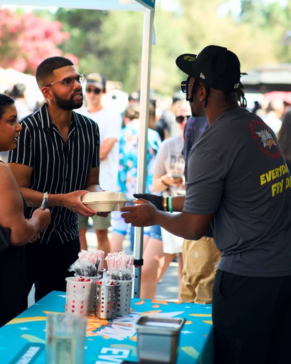 Two men talking at a food truck serving window outdoors on a sunny day