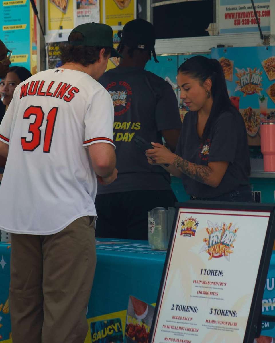 Guests in jerseys standing near a food truck window beside a framed menu board