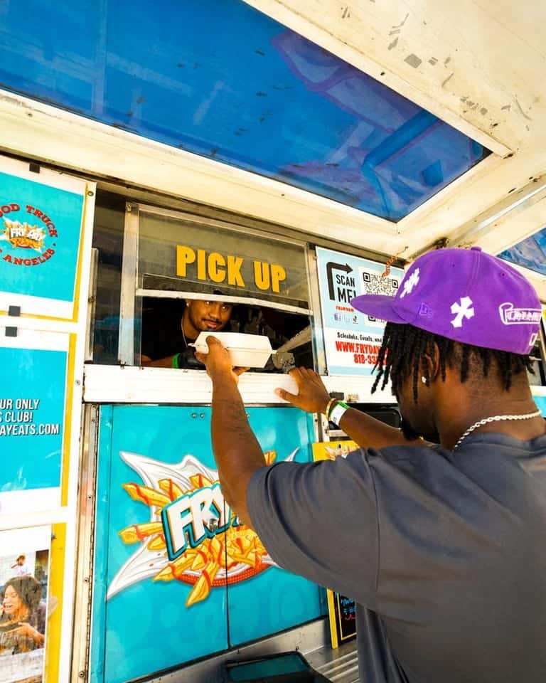 A person in a purple cap reaching toward the pickup window of a turquoise food truck