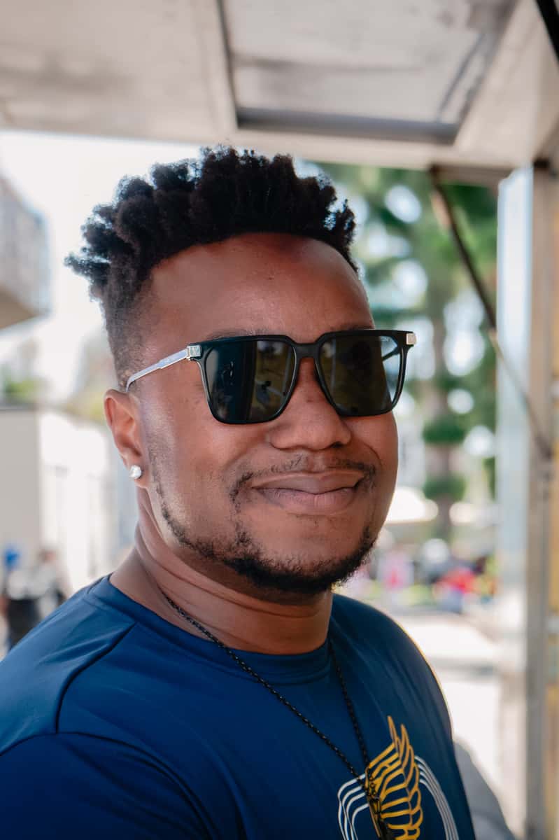 Smiling man wearing sunglasses and a navy shirt, photographed outdoors in daylight