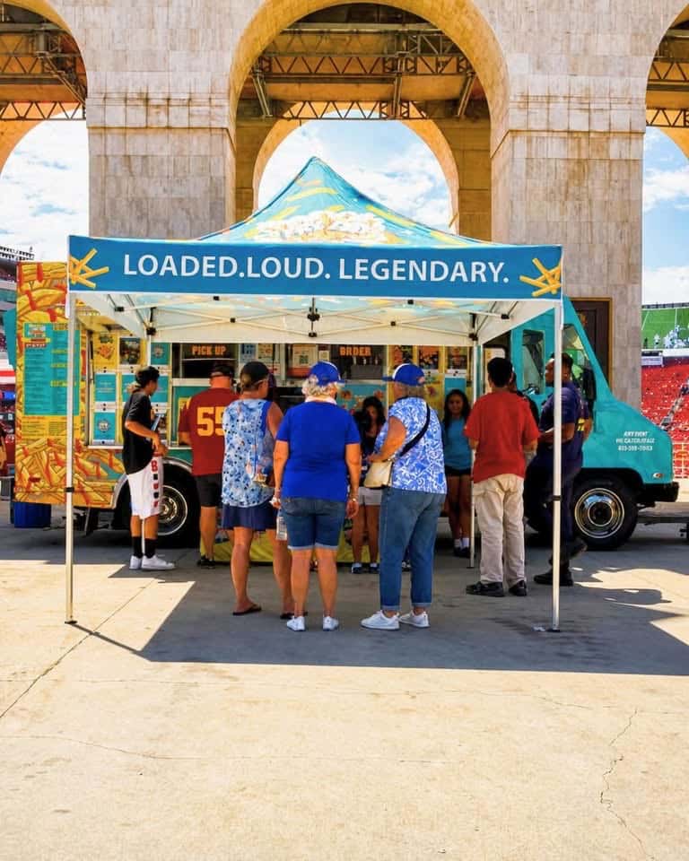 A group of people standing in line at the window of a food truck outdoors
