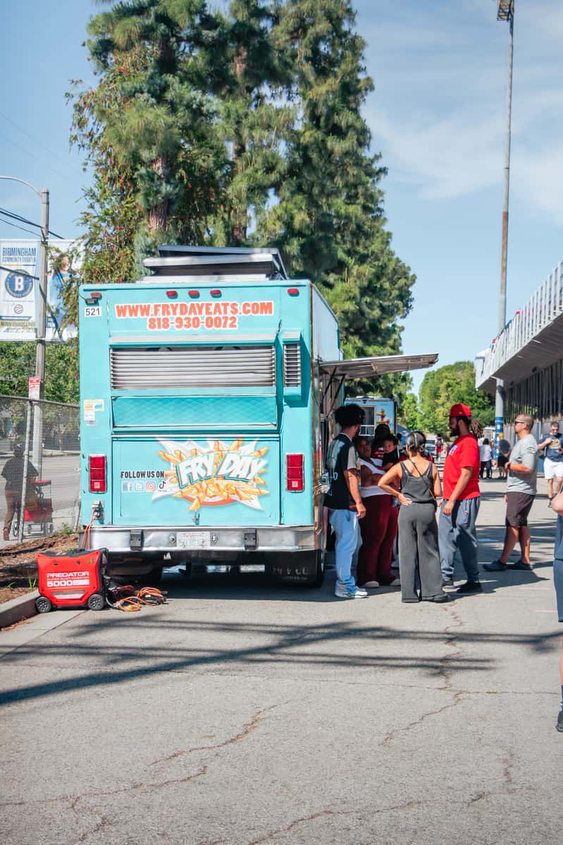 Teal and white food truck parked on a street with a small group of people standing near its serving window