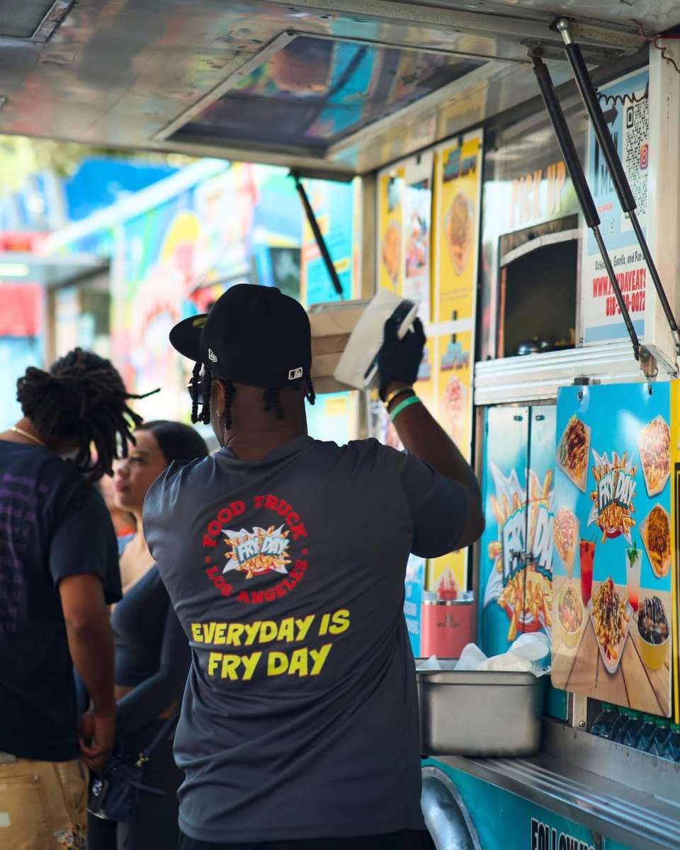 Person in a black cap standing at a colorful food truck at an outdoor event