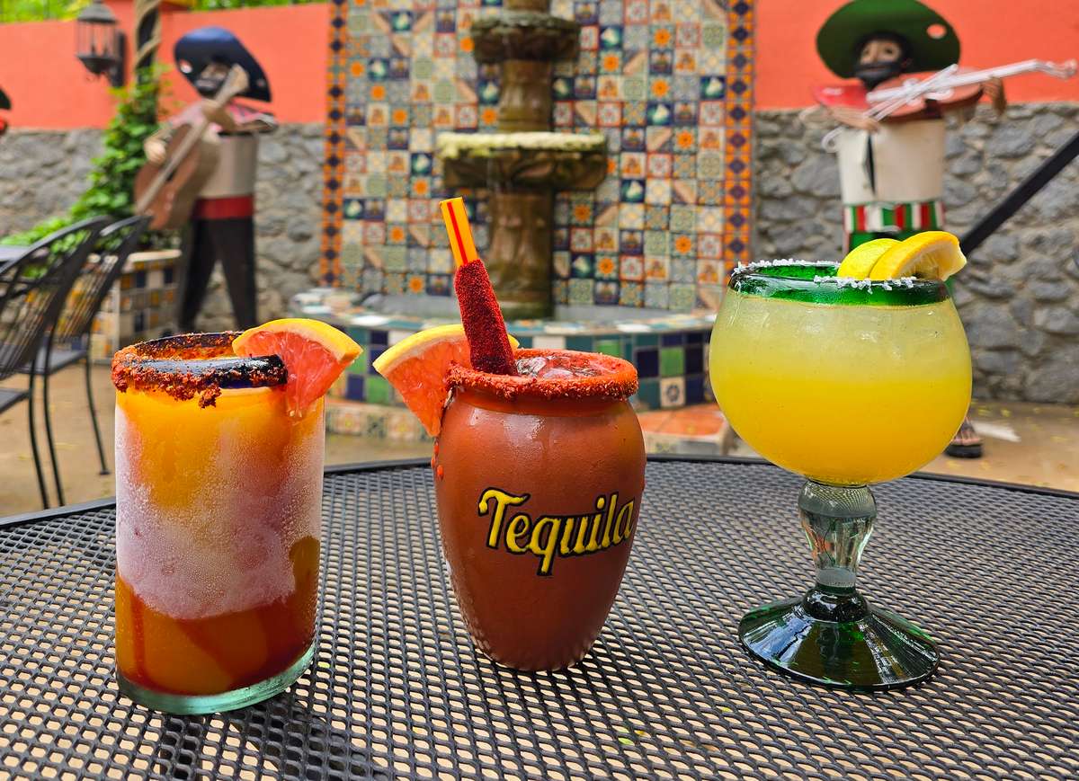 three cocktails showing in outdoor seating area with stone fountain