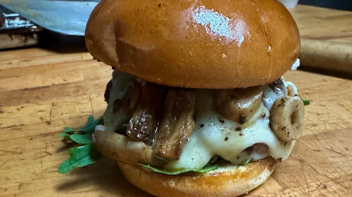 Burger with sautéed onions, melted cheese, and greens served on a toasted bun