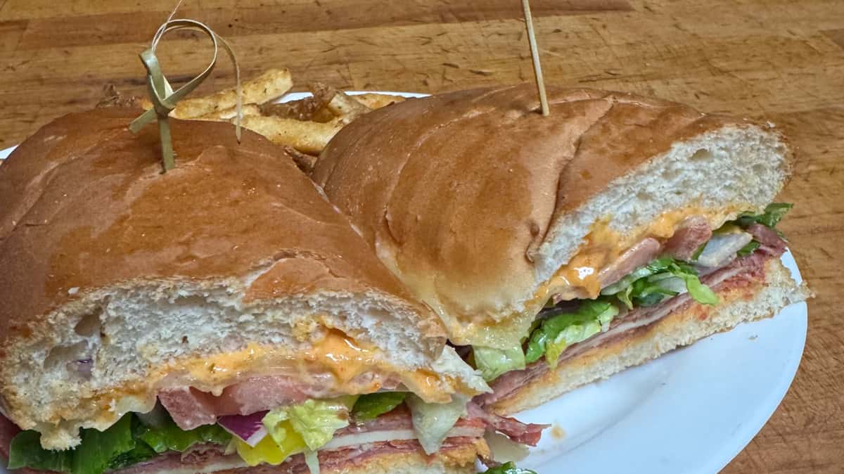 Italian sub sandwich cut in half, filled with deli meats, cheese, lettuce, and tomatoes.