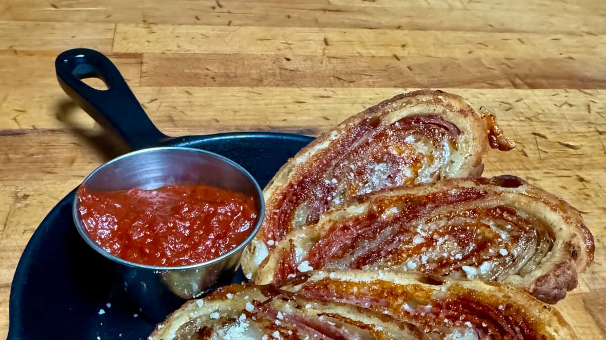 Sliced pizza bread served with a side of marinara sauce on a wooden board