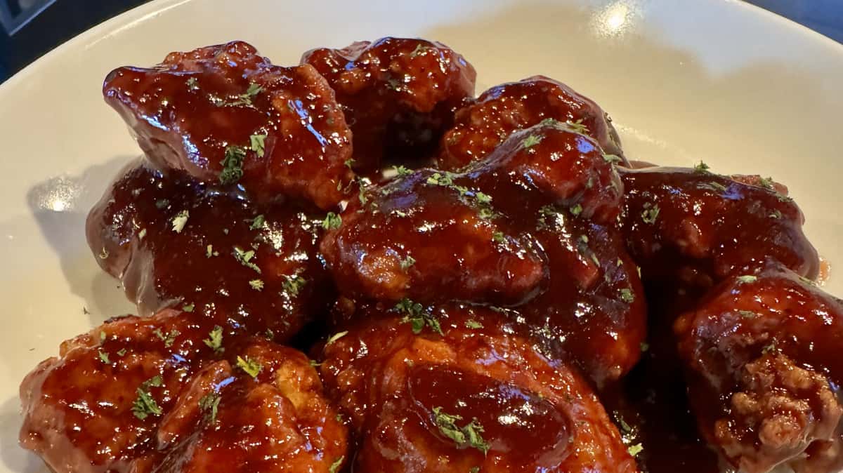 Crispy chicken wings coated in a glossy barbecue sauce, garnished with herbs.