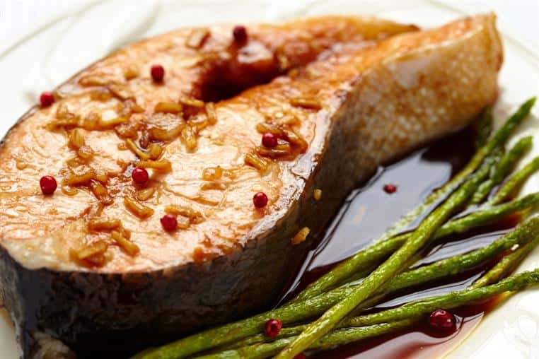 a slices of fish with seasoning and herbs in brown soup on a plate