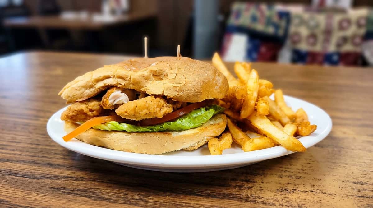 Fried chicken sandwich with lettuce, tomato, and crinkle-cut fries on a white plate.