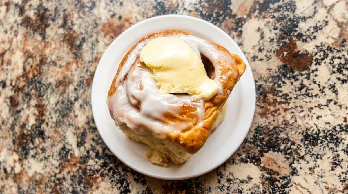 Cinnamon roll with white icing and a pat of butter, served on a white plate.