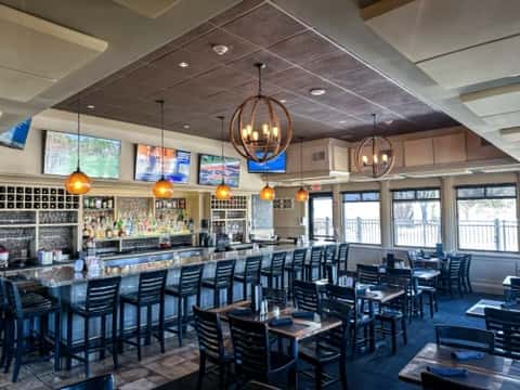 Carmela's bar and lounge has black wooden chairs, high ceilings with hanging wooden chandeliers, and granite bar with multiple televisions.