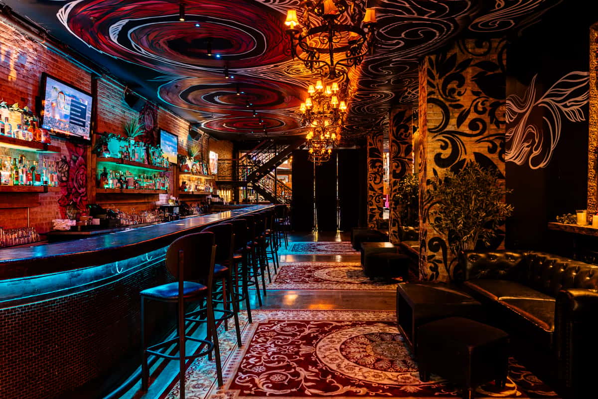 Ornate bar with swirling ceiling art, chandeliers, velvet seating, and a moody, upscale atmosphere.