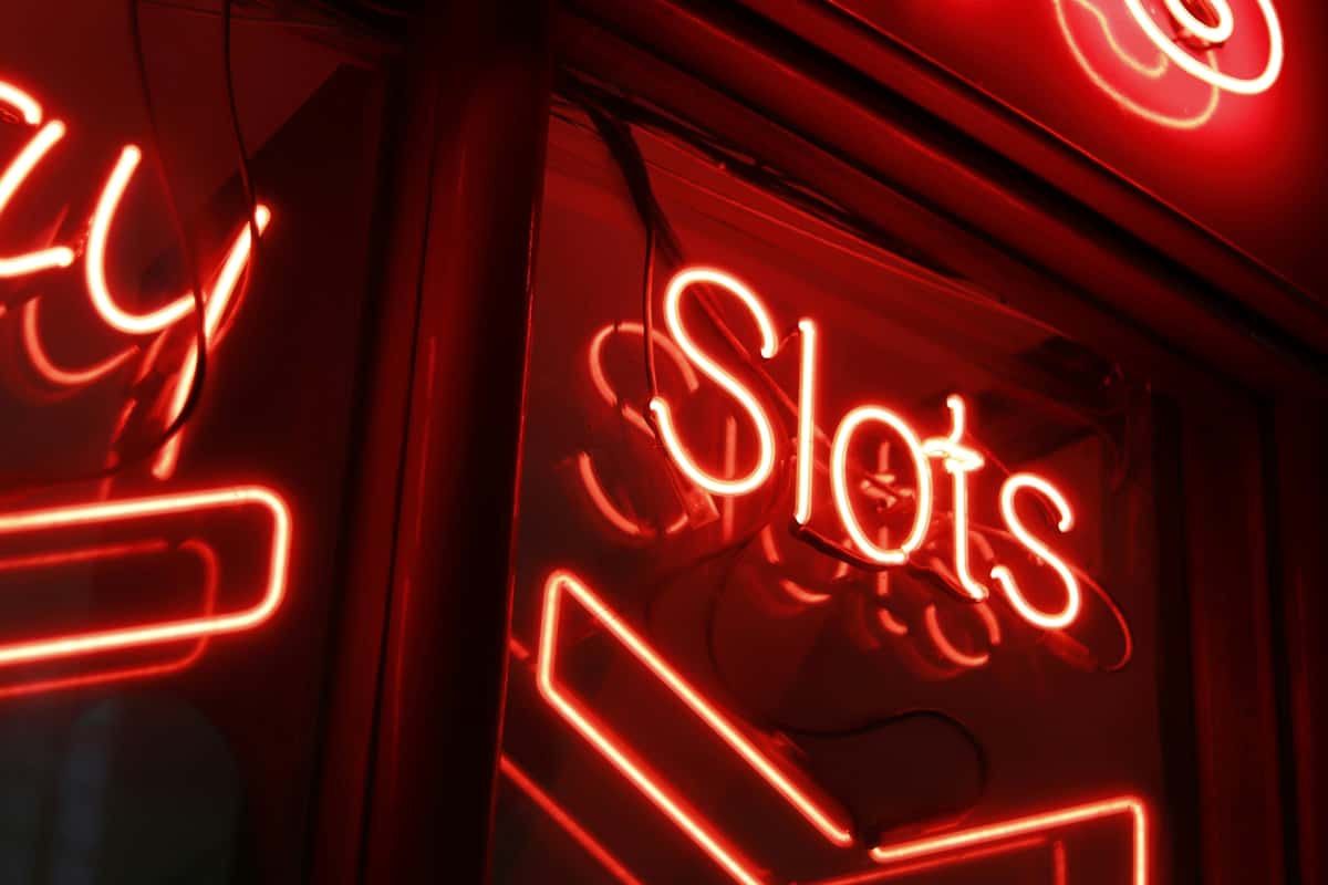 Red neon sign glowing with the word "Slots," reflecting a casino or gaming atmosphere with vibrant lighting.