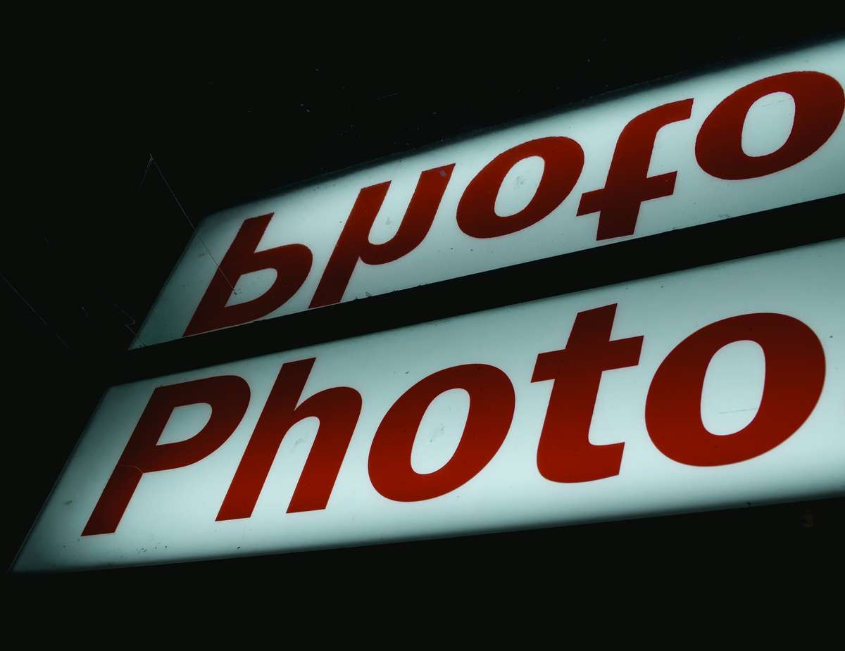 Illuminated sign with the word "Photo" in bold red letters, with the reflection showing reversed text.