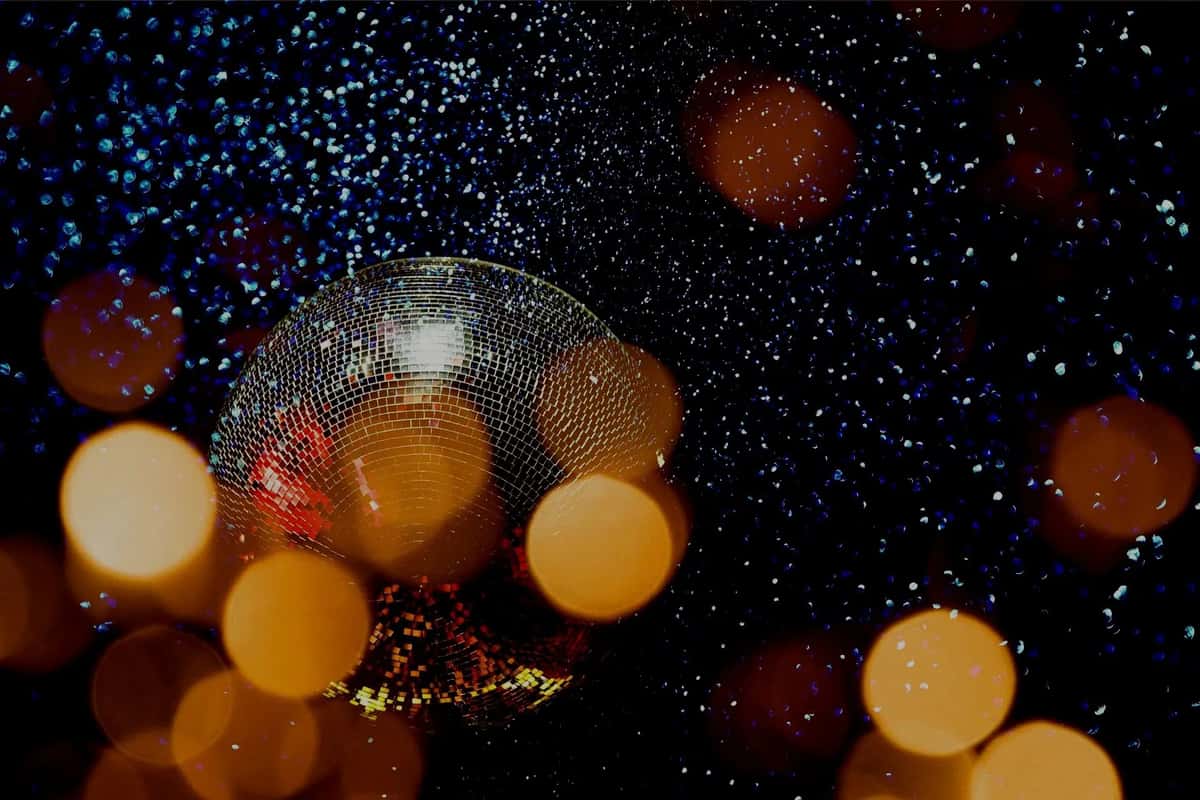 Disco ball reflecting colorful lights with golden bokeh and sparkling specks against a dark, festive background.
