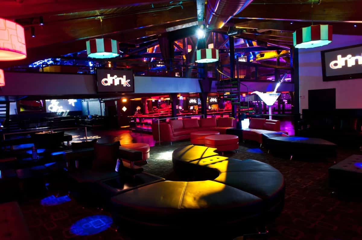 Colorful nightclub lounge with vibrant lighting, modern seating, and illuminated decor, including "drink" signs on the walls.