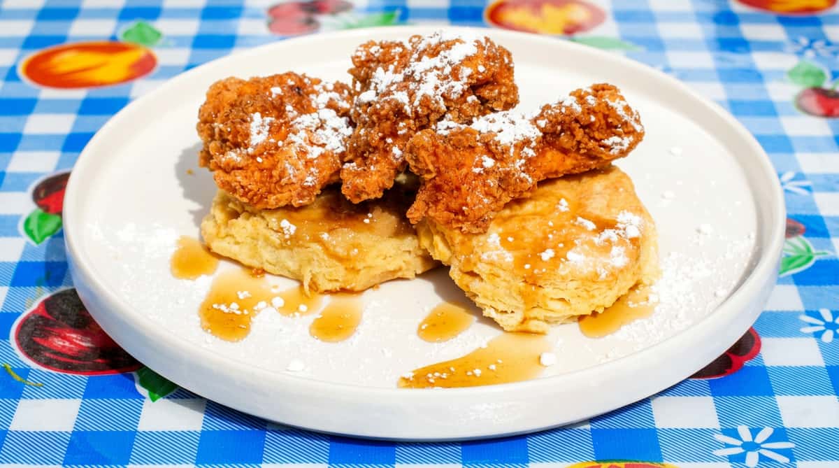 Fried chicken tenders on two biscuits, drizzled with syrup and powdered sugar, on a white plate.
