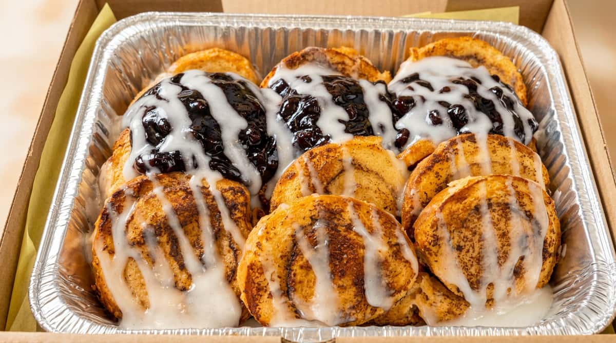 Monkey bread in a foil pan, with brown sugar glaze, white icing, and a row of dark fruit topping.