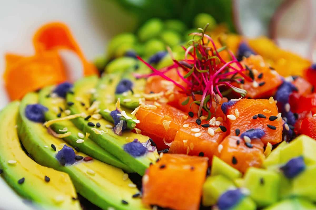Fresh salmon poke bowl with avocado, edamame, sesame seeds, lime, and colorful microgreens